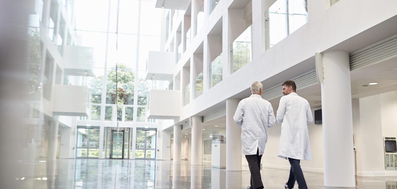 Rear View Of Doctors Talking As They Walk Through Hospital