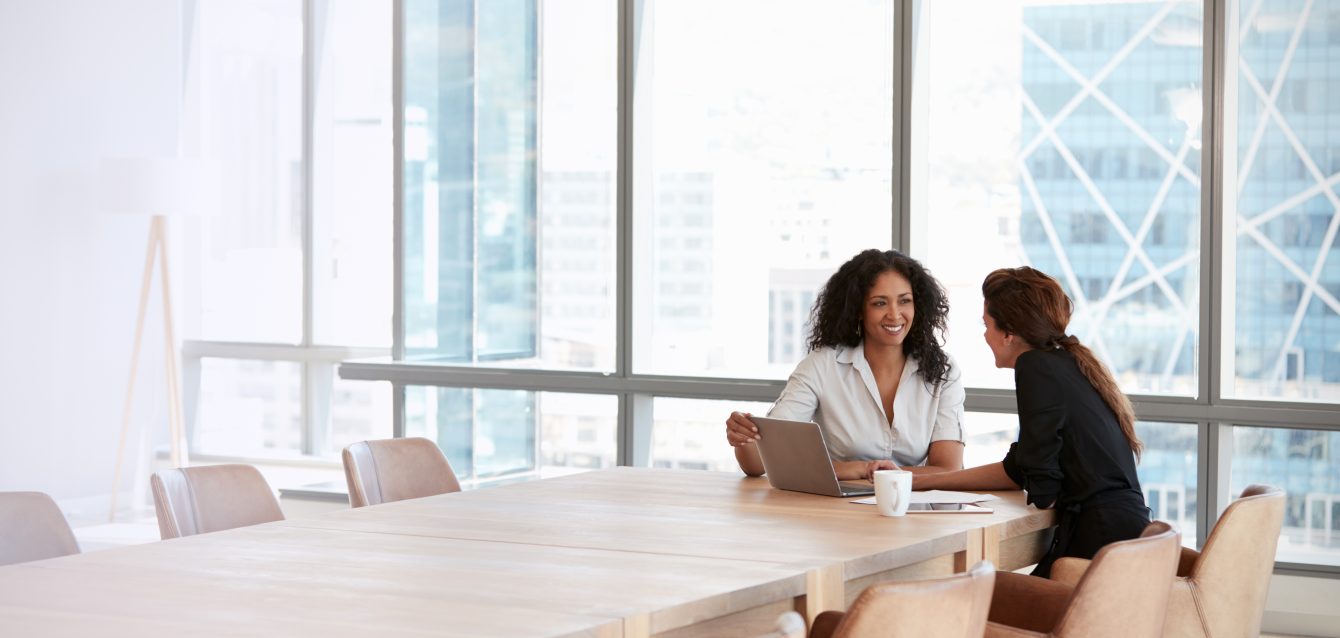 Two Businesswomen Using Laptop In Boardroom Meeting